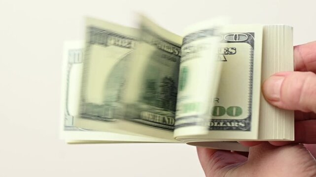 Close-up of hands flipping through a stack of 100 dollar bills on a white background. Hands counts money