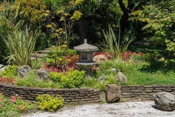 Quiet garden with a traditional stone lantern surrounded by lush greenery, palm trees and winding stone path. Japanese Garden or Russian-Japanese Friendship Garden in Sochi.