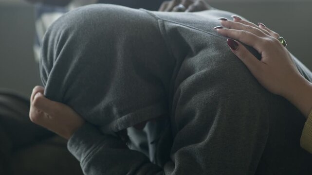 Side view shot of unrecognizable hand patting on shoulder of depressed person covering face with hood, showing empathy and support