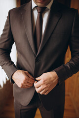 Close-up of a groom in a brown suit buttoning his jacket before the wedding ceremony. Elegant men&rsquo;s formalwear, preparation moment, stylish groom attire, and wedding morning details.
