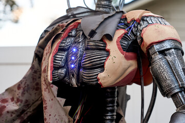 Detailed view of a cyborg torso showing metallic ribs, glowing blue diodes, and tattered skin. Mechanical cables and armor plating form a spooky Halloween decoration by a house.