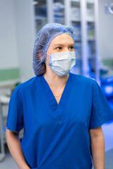 Female nurse in scrubs. Nurse in blue scrubs and protective mask standing in the operating room