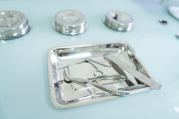 Sterile metal surgical instruments on a tray in a medical facility. Close-up view of shiny metal surgical instruments placed on a stainless steel tray in a clinical environment.