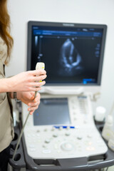 Medical professional preparing ultrasound examination. A healthcare worker holding an ultrasound probe in front of a diagnostic screen with a heart image.