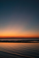Fototapeta premium Tranquil seascape at sunset with vivid orange and blue gradient sky reflecting on calm ocean waves