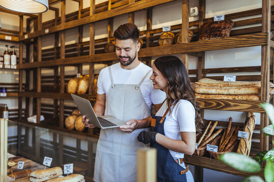 Bakery Team Reviews Orders On Laptop Inside Cozy Bread Shop As Fresh Breads Shine
