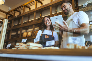 Happy Bakery Staff Using Tablet Behind Fresh Bread Display in Cozy Modern Bakery Shop