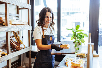 Smiling Bakery Worker Preparing Fresh Sandwiches in Bright Bakery Shop With Bread on Shelves