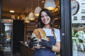 Smiling Woman Bakery Worker Holds Fresh Loaf at Cozy City Cafe Entrance