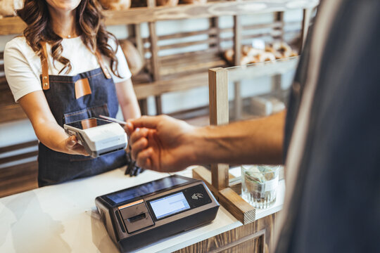 Smiling Cashier Hands Card Reader to Customer at Bakery Checkout in Busy Store