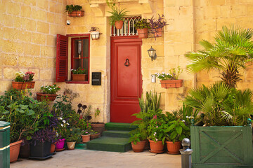 Cozy courtyard with a red door, shuttered window, and green potted plants in the street of an old Mediterranean town.