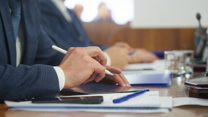Businessman in suit using digital tablet with stylus during meeting, close-up of hand and modern technology in corporate work process. Photo
