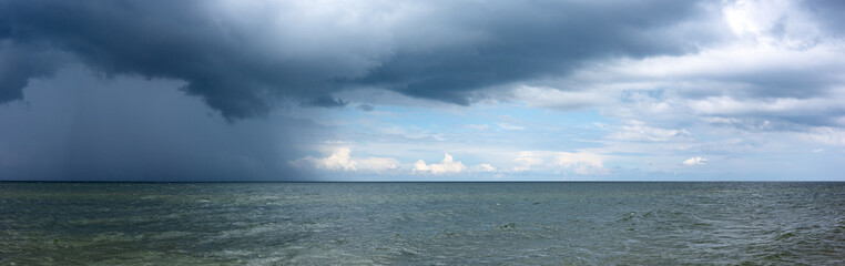 Heavy, dark storm clouds gather over the sea horizon. Green, calm waters before an approaching weather change.