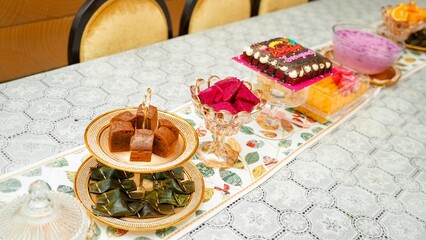 Festive dessert table featuring assorted Malaysian kuih, banana leaf parcels, chocolate cake slices, dragon fruit cubes, and a decorated birthday cake arranged on elegant plates and stands
