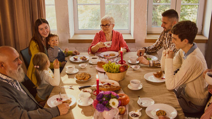 Family gathering around table sharing tea and pastries in warm atmosphere. Concept of home traditions, intergenerational bonding, lifestyle branding, emotional storytelling, and seasonal happiness.