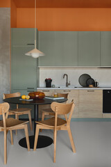 Modern kitchen with green cabinets, wooden fronts, black round dining table and natural wood chairs under pendant light.