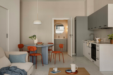 Open-plan living space with grey kitchen cabinets, round dining table and orange chairs.