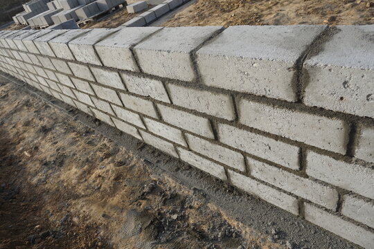 Fototapeta Murowanie fundamentu widziane lekko z góry pod kątem. Bloczek po bloku układana zaprawa, staranna i solidna praca murarska na placu budowy.