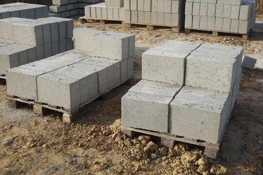 Fototapeta Bloczki budowlane ułożone na paletach, w tle widoczna budowa i kolejne stosy bloczków. Przemysłowy i budowlany krajobraz placu budowy.