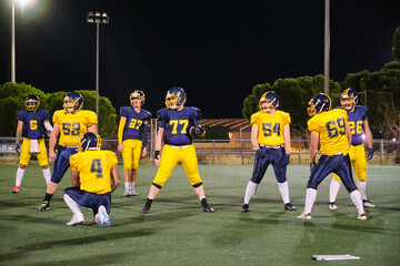 American football team practicing sport maneuvers on an illuminated field after dark