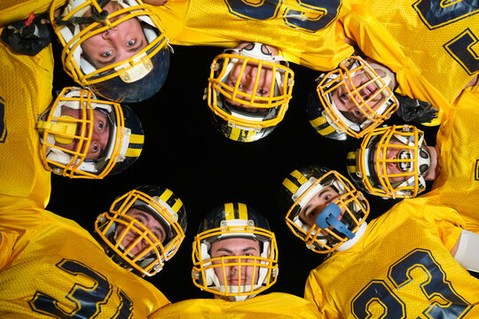 American football team members in yellow jerseys and helmets huddling together