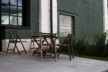 Modern outdoor space with foldable wooden chairs and table against an industrial style building. The contrast of green and white walls creates calm, minimalist atmosphere for relaxation