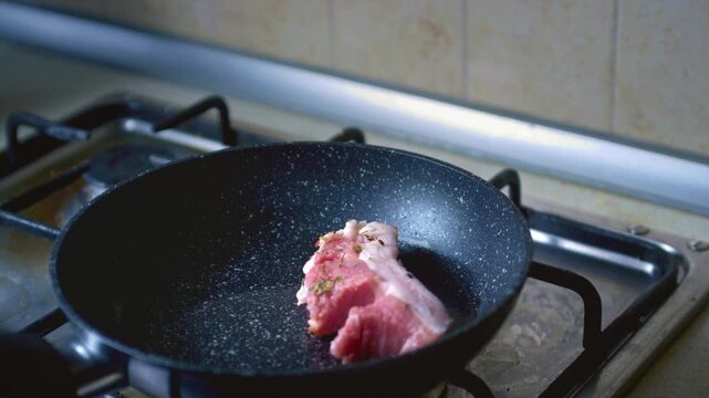 Chef hand cooking smoked grilled pork on iron grill pan. Cooking a pork at home. Prepares ingredients for a Peruvian dish pan con chicharron. Raw pig meat in the kitchen. Flips the pieces with a fork