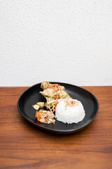 Traditional Indonesian food served on a black plate. Steamed white rice with chicken, vegetables, and sambal matah.