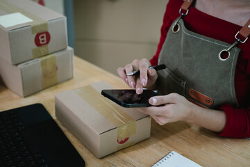 A person using a smartphone and holding a pen while working with packages, symbolizing e-commerce, online business, and order management.