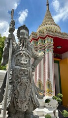 Stone guardian statue stands resolute beside ornate pagoda, embracing spiritual festivity of Songkran and Ghost Festival reverie
