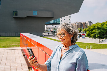 Happy senior woman using smartphone in city connecting
