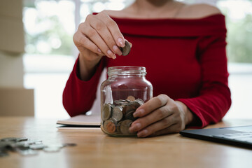 A woman placing coins into a glass jar, symbolizing savings, money management, financial planning, and economic responsibility.