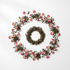Artistic composition of dried green tea leaves and delicate pink rose petals arranged in two circular wreaths, creating a visually appealing and organic design against a clean white background .