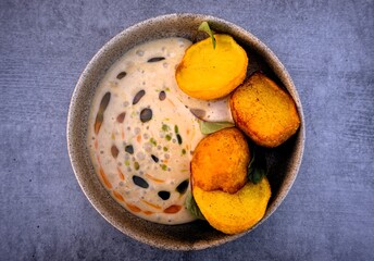 Roasted potato slices as appetizer with creamy sauce in ceramic bowl on gray background.