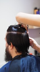 Fototapeta premium Hairstylist attaching a new capillary prosthesis to a man's head sitting on a salon