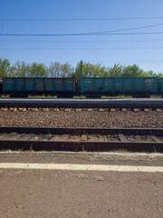 Freight train cars parked on railway tracks under a clear blue sky, surrounded by green trees, showcasing the industrial landscape and transportation concept