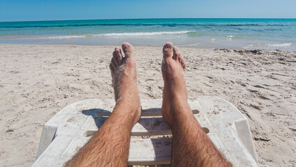 A man's legs with sand on them on a sunbed on a sandy beach. Relaxation on a beach. Man's legs with...