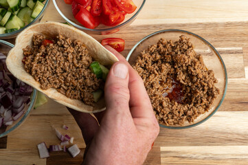 Hand holding tortilla with ground meat and vegetables
