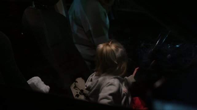 Child embarks on quiet night journey within dimly lit car interior, engaging with gadget amidst profound darkness and motion.