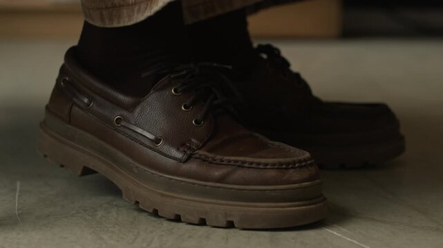 Cropped close up shot of legs in brown shoes of unrecognizable person shaking because of anxiety or neurological disease