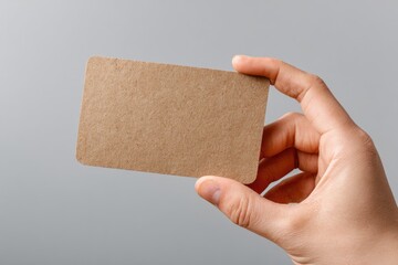 A light brown card held in a hand against a gray background.  Close-up shot, showing the blank card clearly.  Natural light