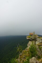 Wysokie skały z widokiem na góry w tle, pokryte mgłą. Na szczycie zamontowany drewniany punkt widokowy z barierką, oferujący panoramiczny i malowniczy krajobraz. © Adam