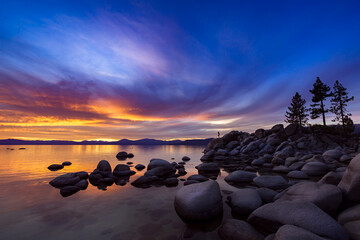 Sunset over lake Tahoe at Sand Harbor. A silhouetted figure is practicing yoga on a rock by the water.