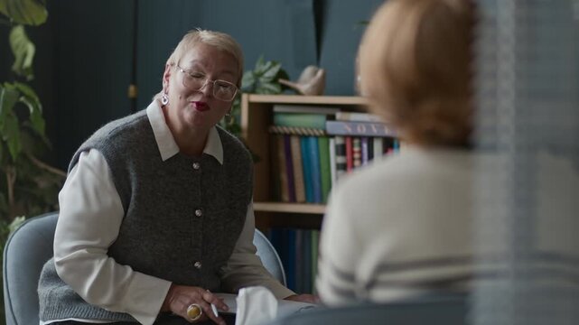 Rack focus shot of middle-aged Caucasian female therapist offering unrecognizable patient in front of her to undergo psychological testing on individual session in modern office