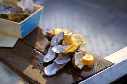 Empty oyster shells and lemon slices on wooden table in sunlight.