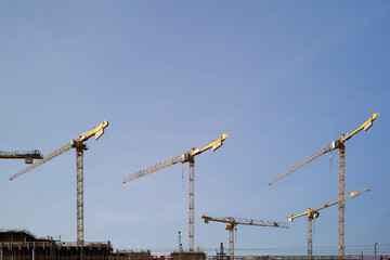 Yellow construction cranes tower against a clear blue sky at a building site. Berlin, Germany