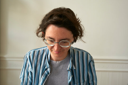 Young woman with glasses and striped shirt looks down against a neutral background. Brussels, Belgium