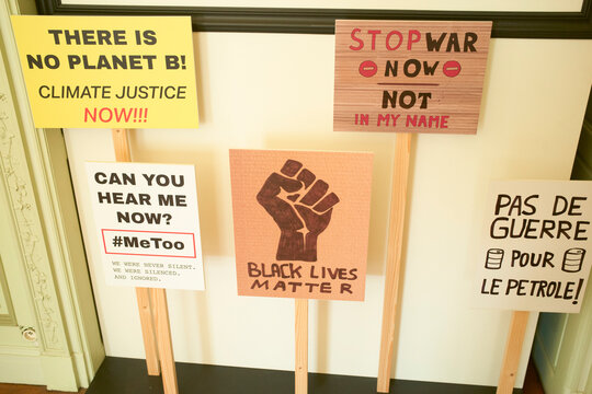 Protest signs demand climate action, equality, peace, and justice on wooden sticks indoors. Brussels, Belgium