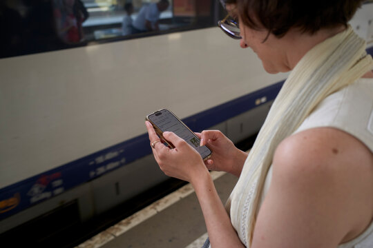 Woman typing on smartphone while waiting by a train platform. Cologne, Germany