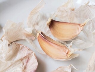 Two garlic cloves surrounded by garlic skin, peel on a light colored surface.